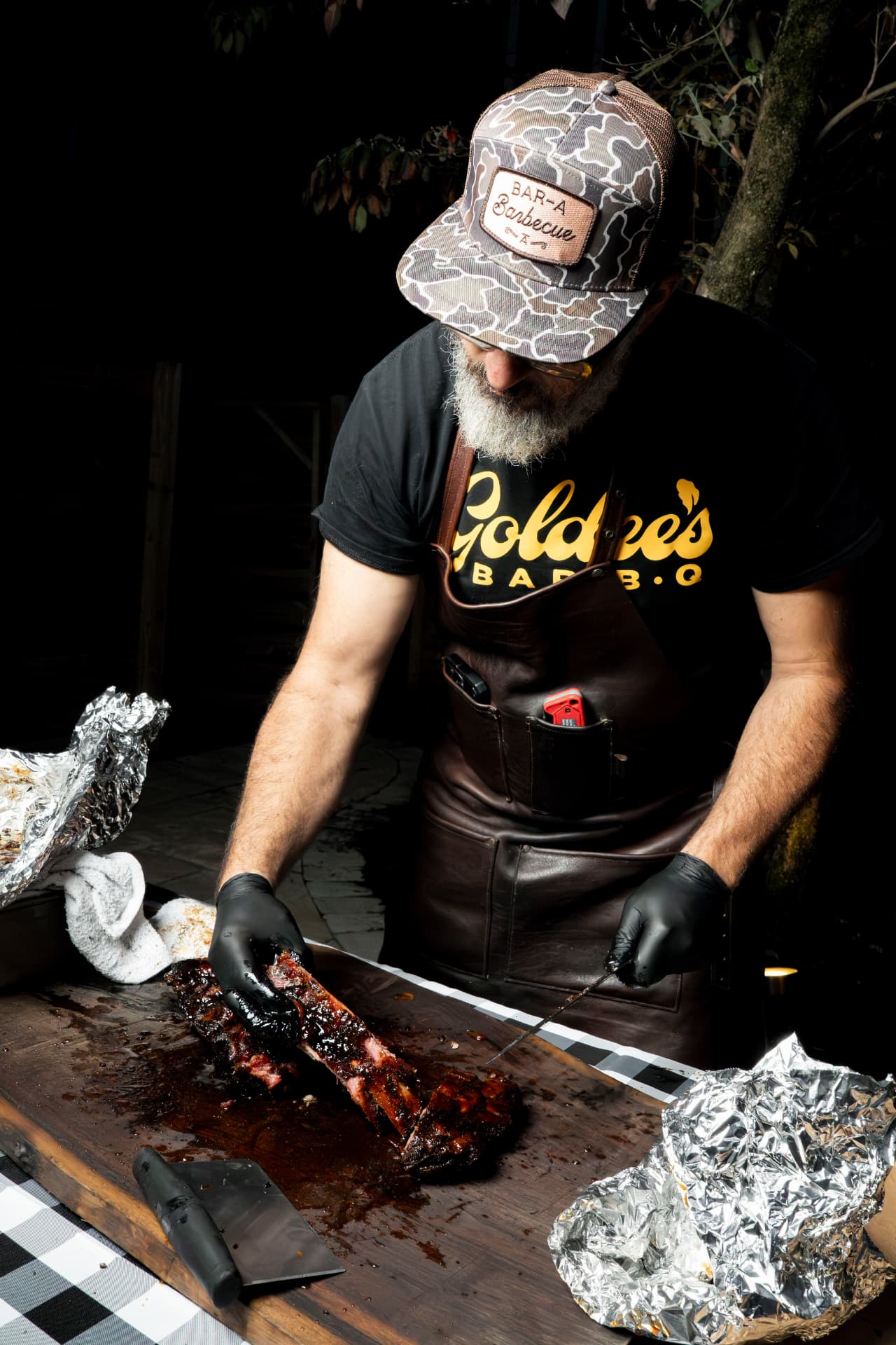 Barbecue pitmaster slicing glazed ribs on a wooden board