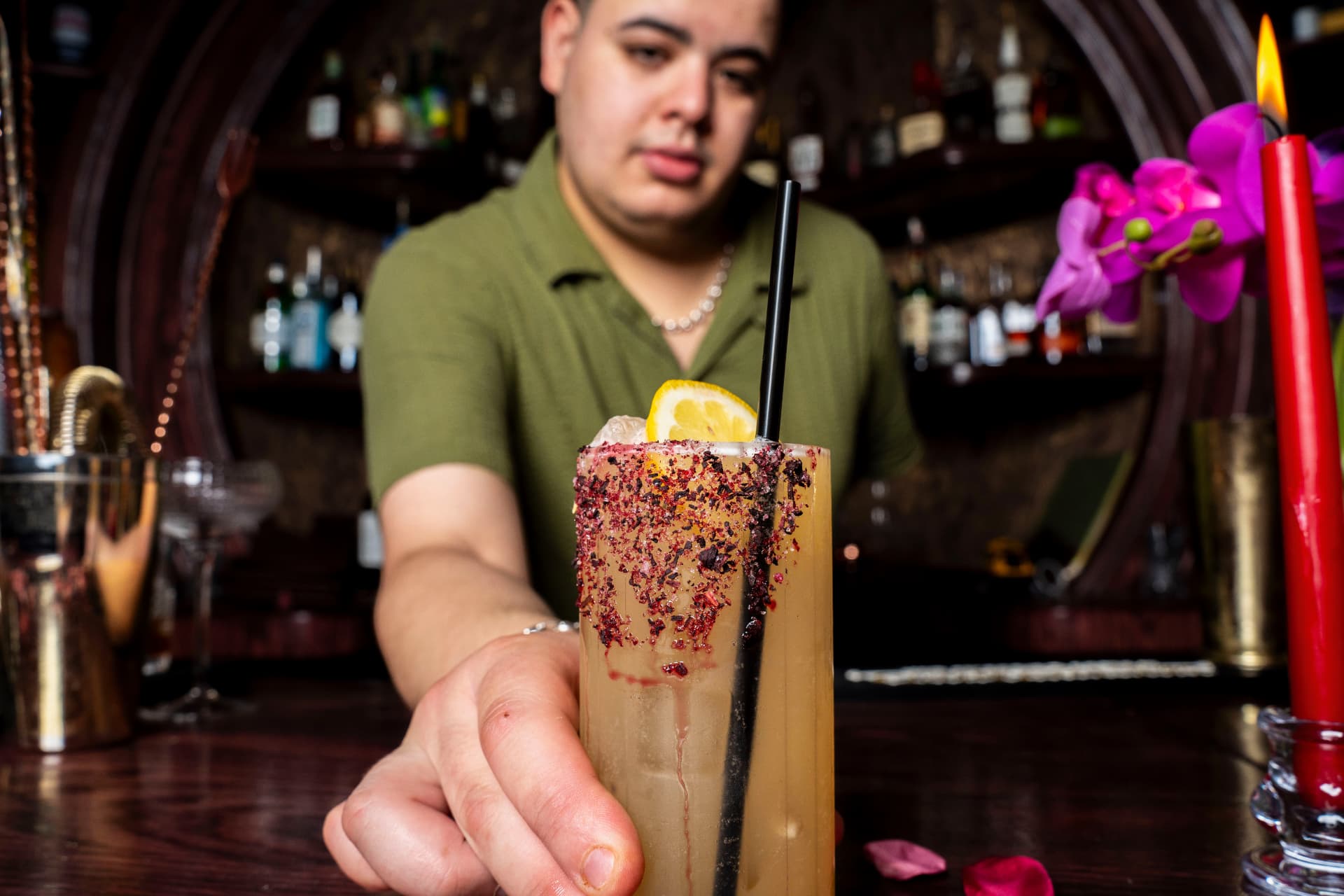 Bartender presenting a finished craft cocktail across a dark bar